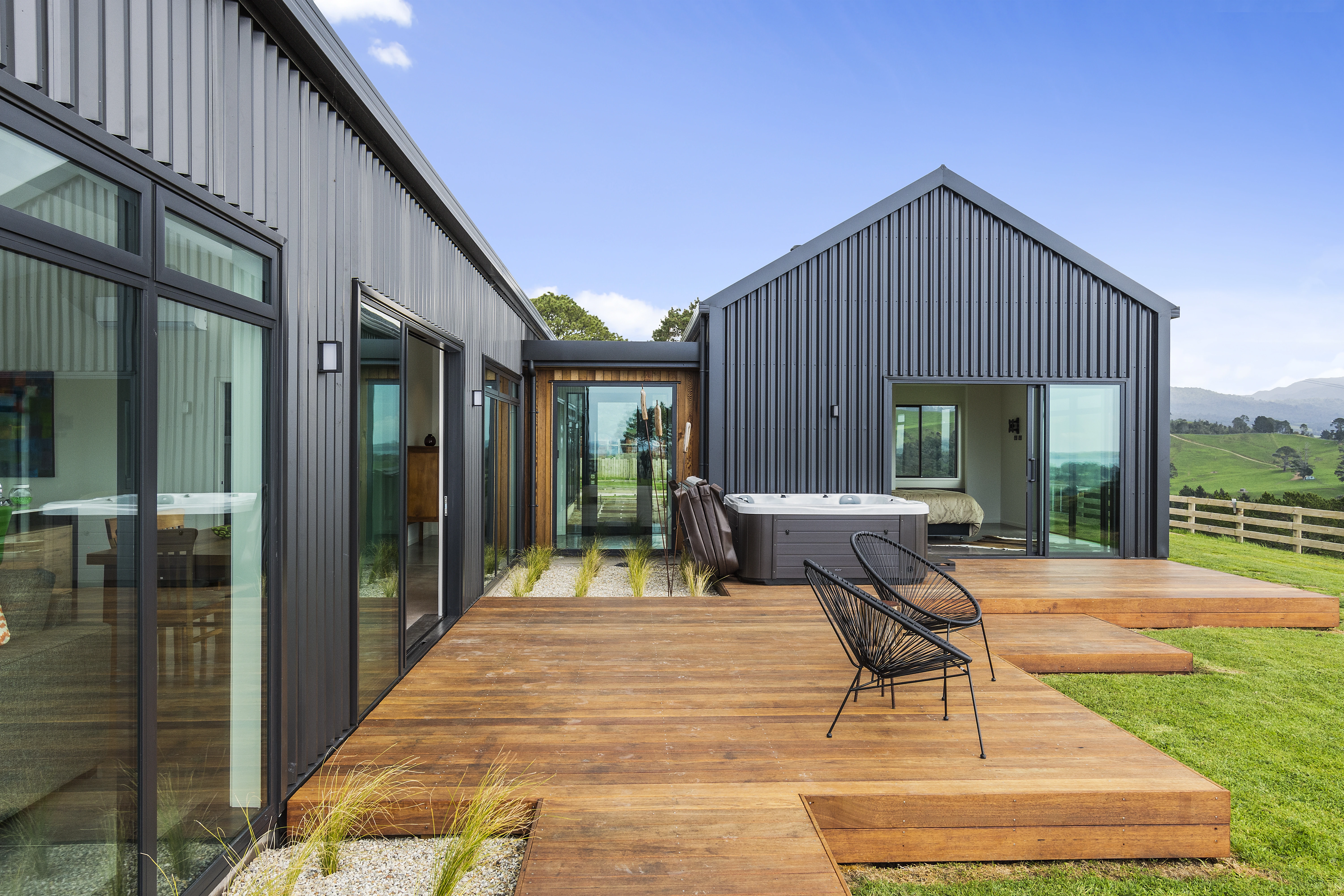 An exterior view of a new home that has new cladding, a new roof and a deck with chairs on it