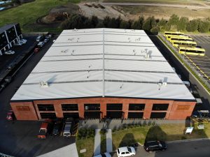 An aerial view of a large commercial building set in an industrial area, with most of the photo showing the new roof