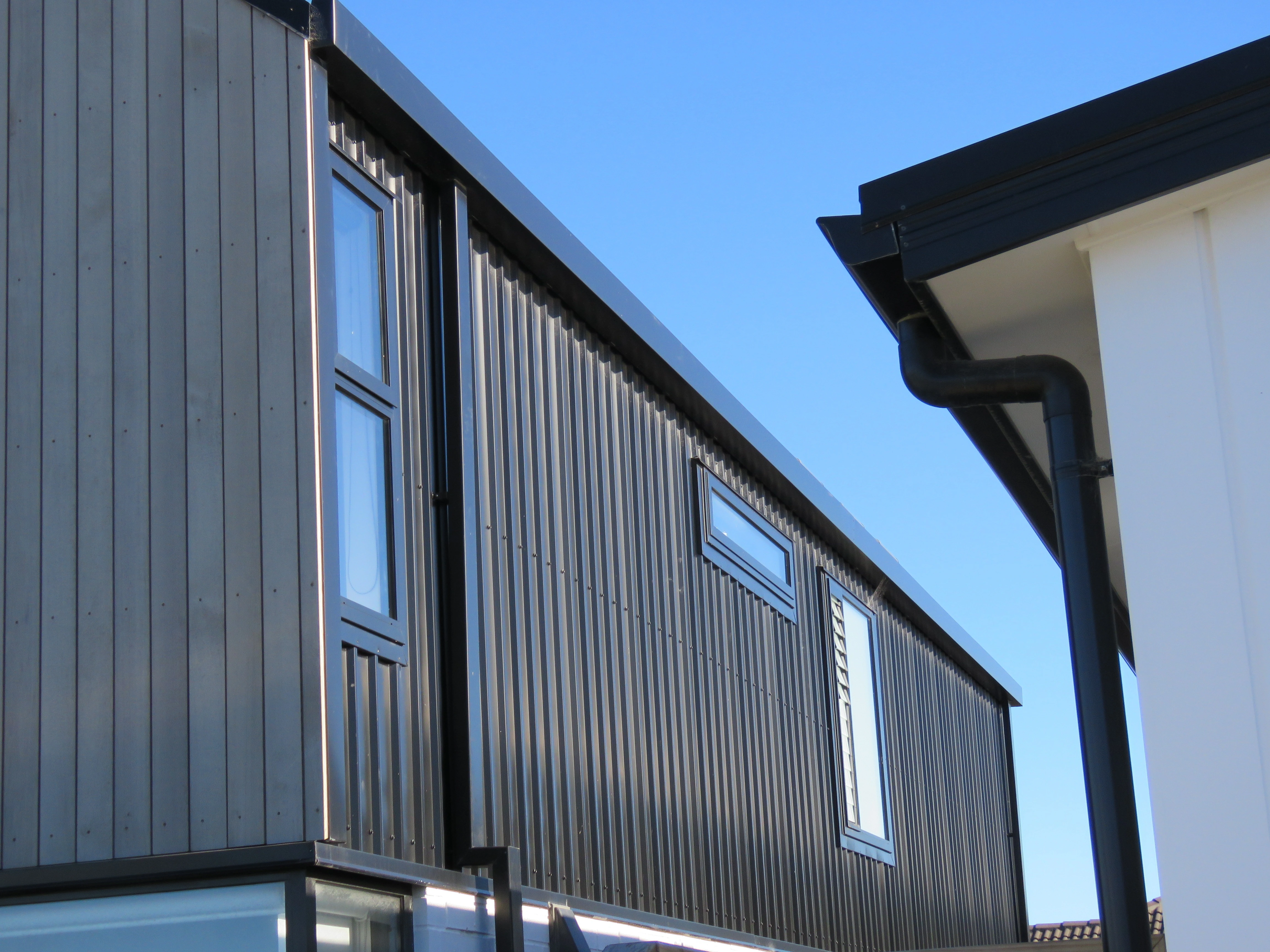 The edge of a house with a new roof, with a new home about three metres away also in frame