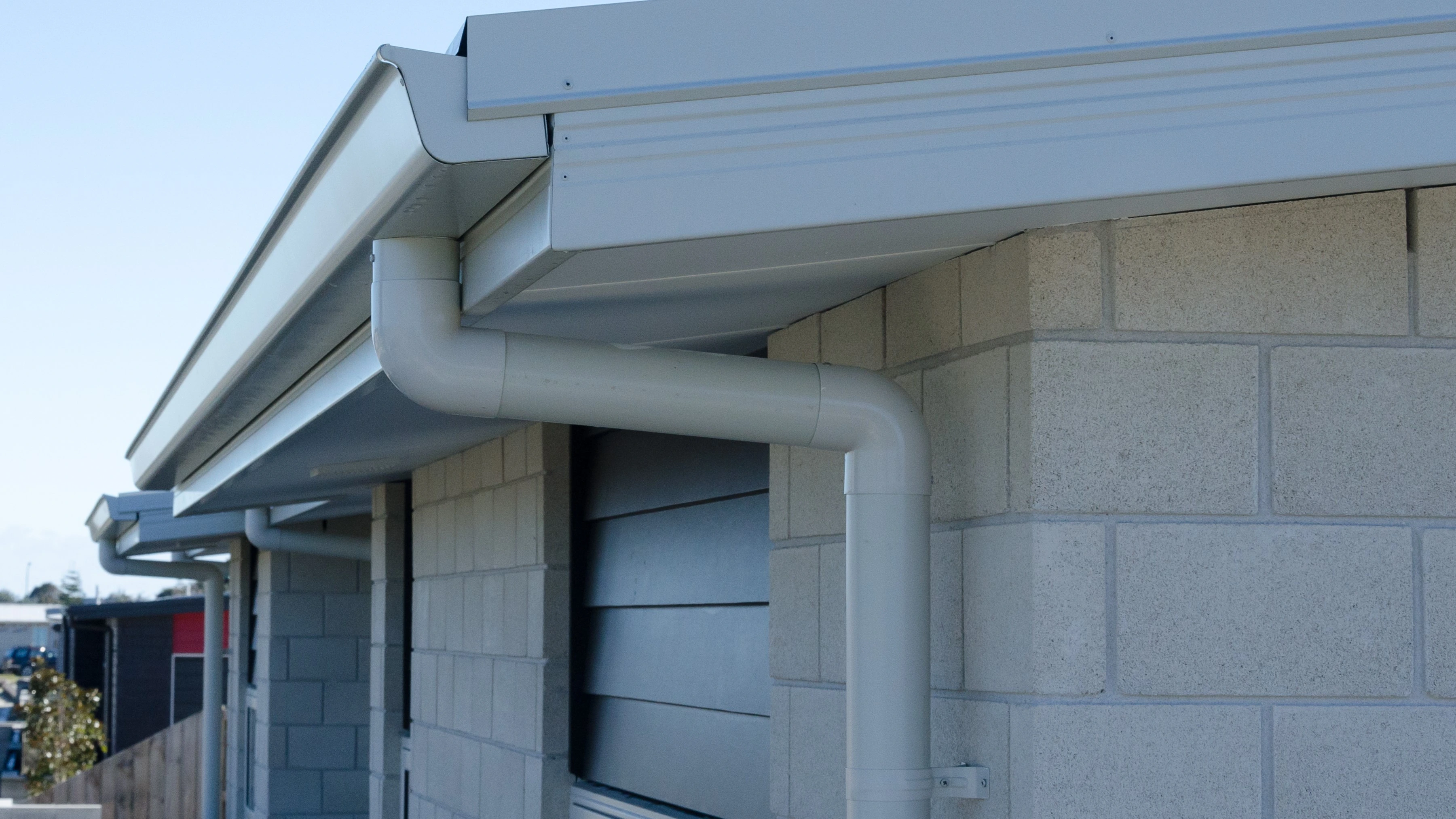 The corner of a house, with downpipes in view, and the corner of a new roof